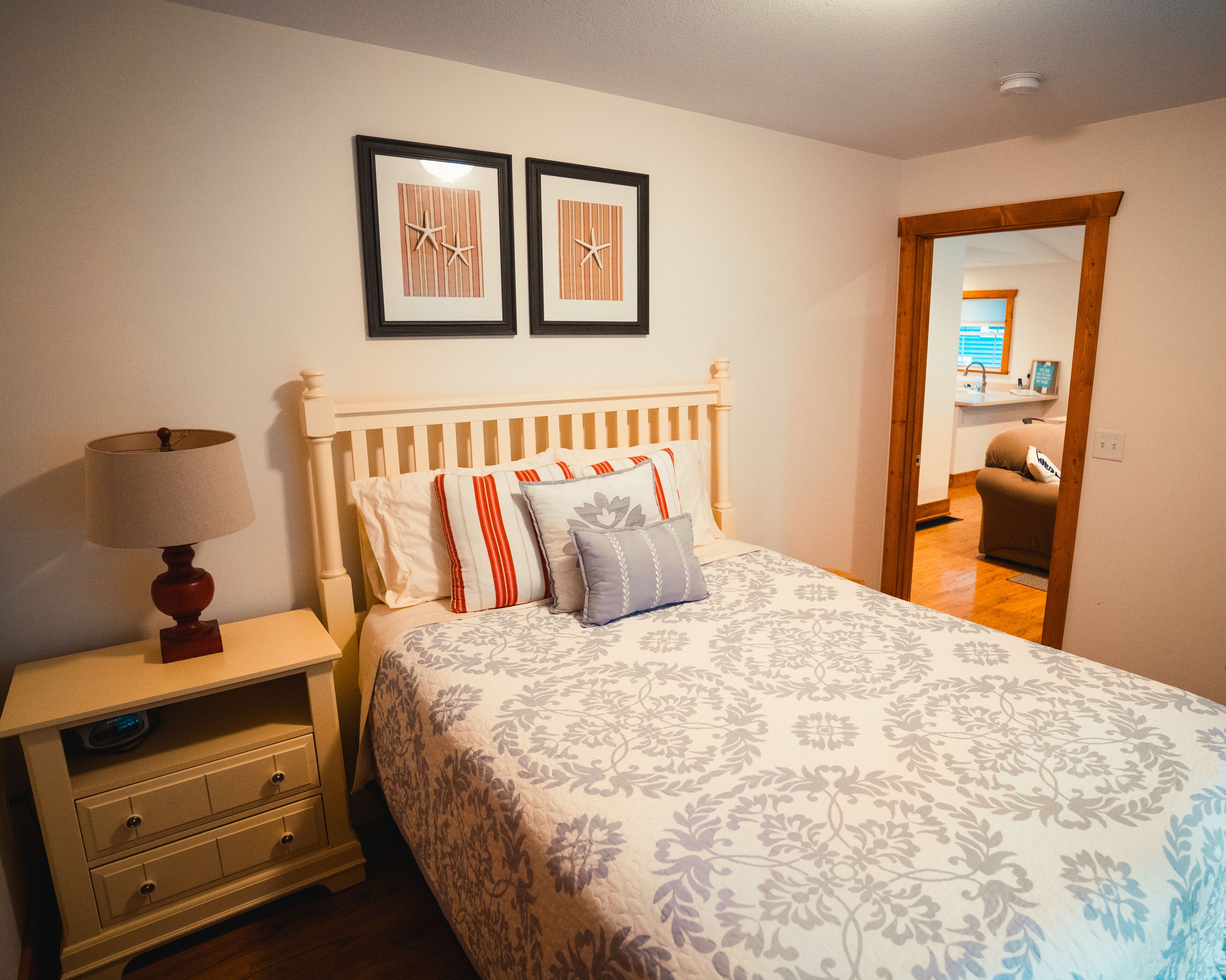 A bedroom with a bed, a nightstand, a lamp, and two framed pictures on the wall.