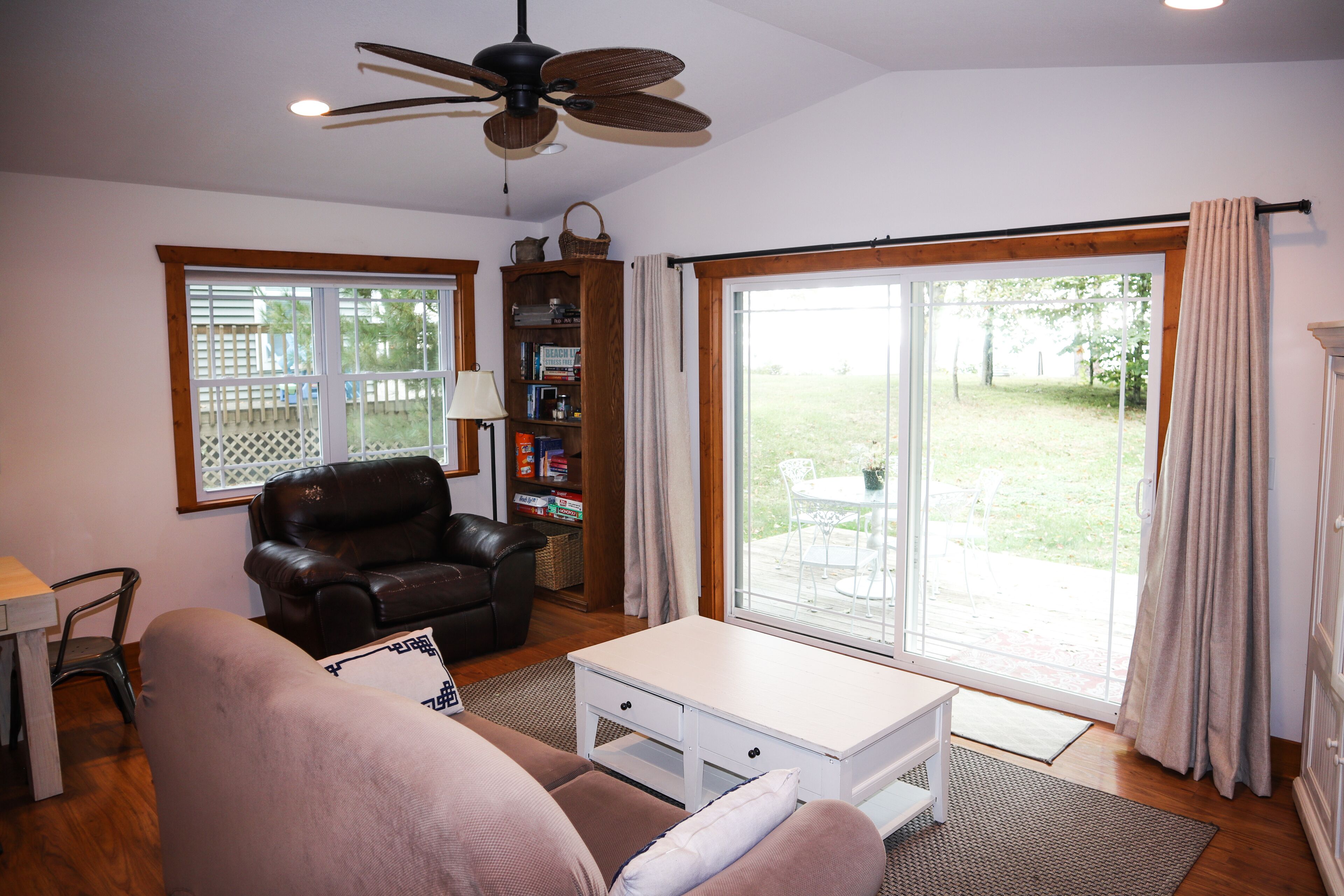 A living room with a brown leather sofa, a white coffee table, a bookshelf, and a sliding glass door to the outdoors.