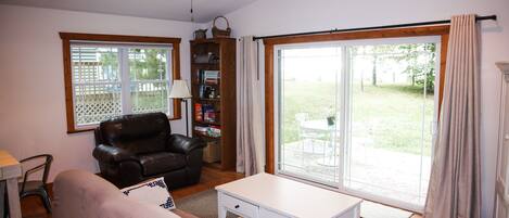 A living room with a brown leather sofa, a white coffee table, a bookshelf, and a sliding glass door to the outdoors.