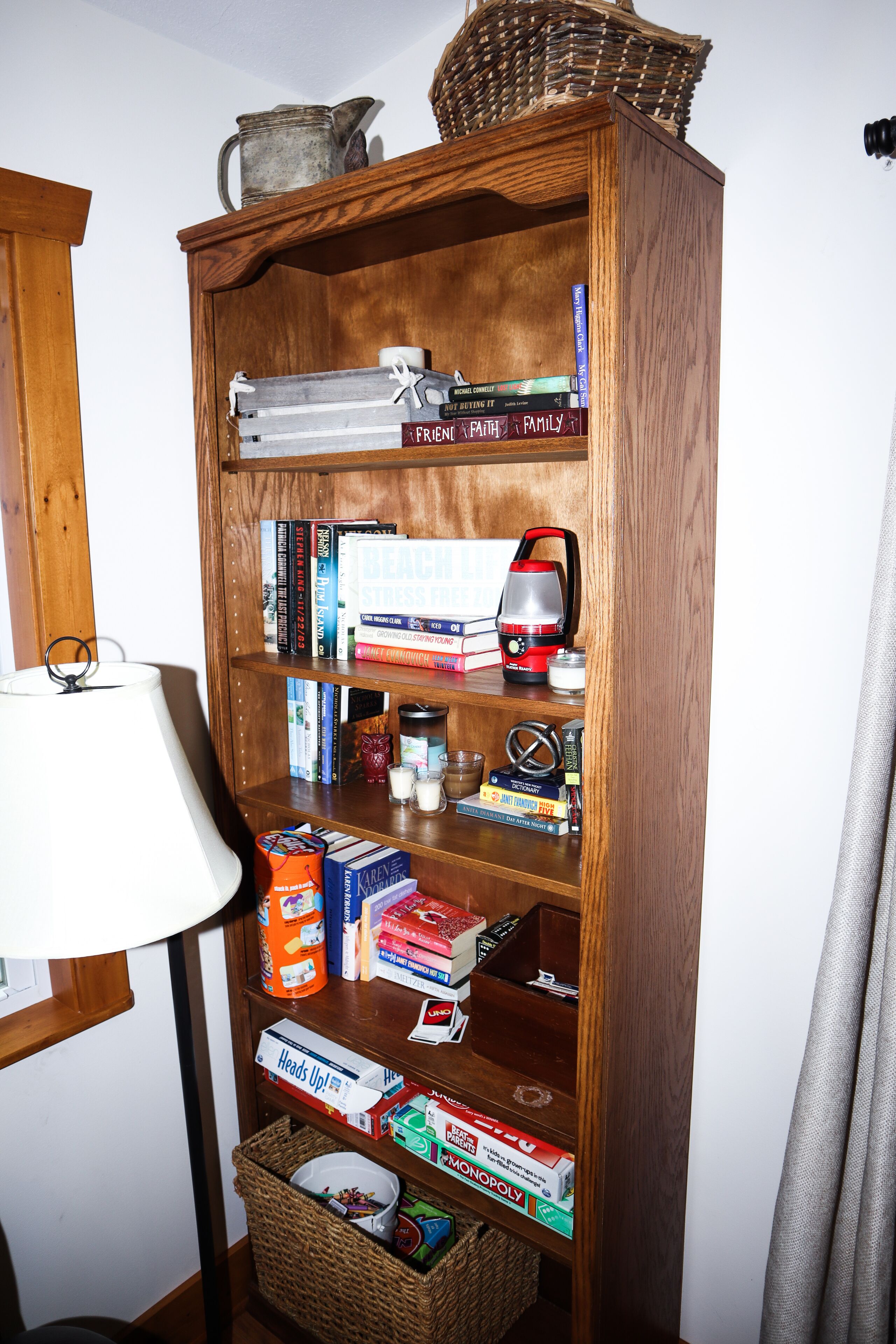 A wooden bookshelf with various books, a red and silver vacuum cleaner, and a wicker basket.