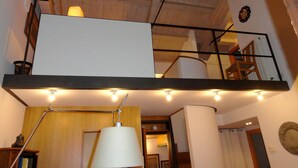 Una habitación con techo de madera, pared blanca y escalera con barandilla de metal.