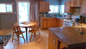 A kitchen with wooden cabinets, a dining table with chairs, a microwave, and a coffee maker. - Peacful and cozy cottage in the mountains (Bigfork)