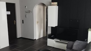 A modern living room with a grey sofa, a black TV stand, and a black wall panel.