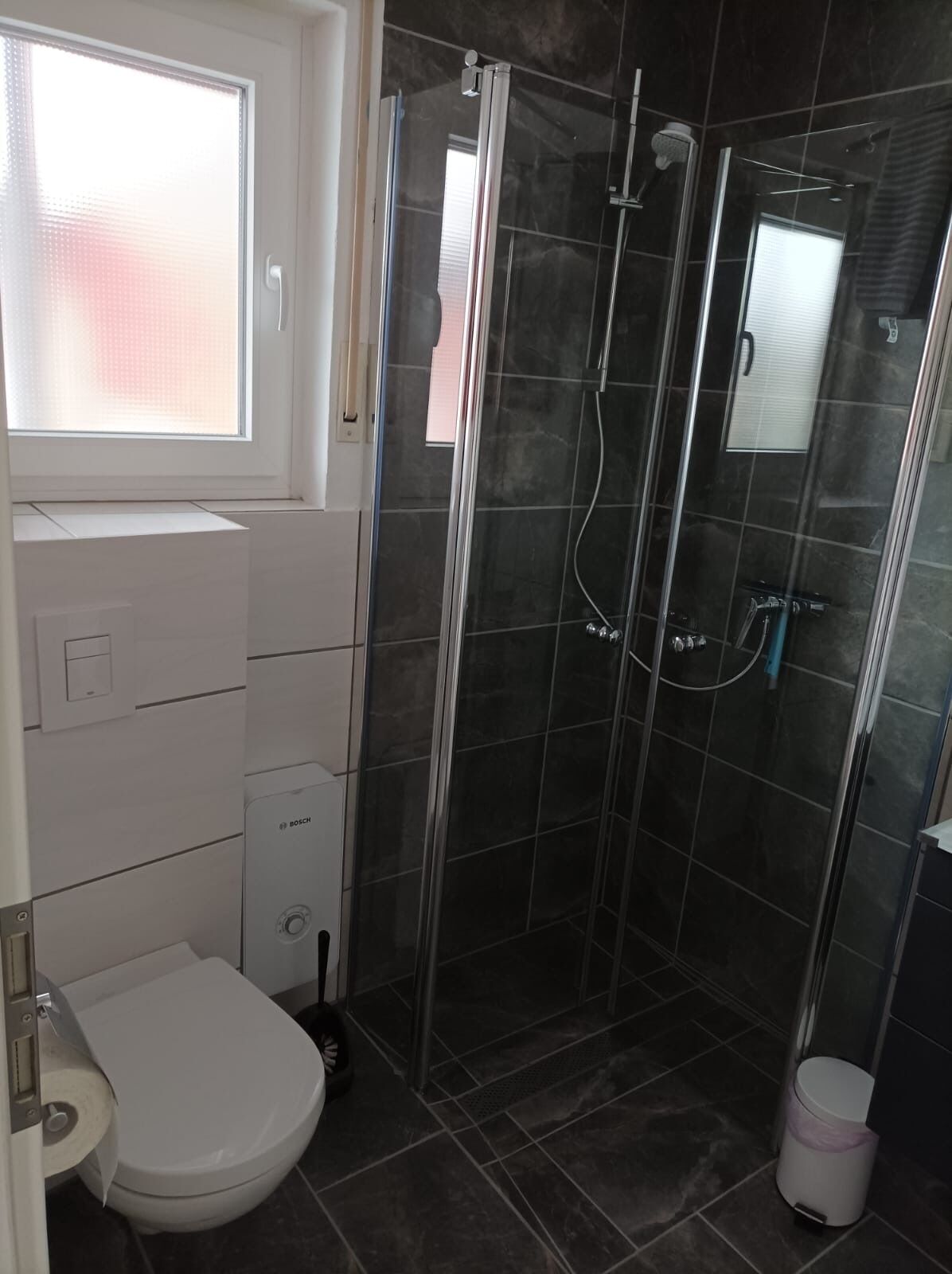 A bathroom with a toilet, a shower enclosure, and a window.