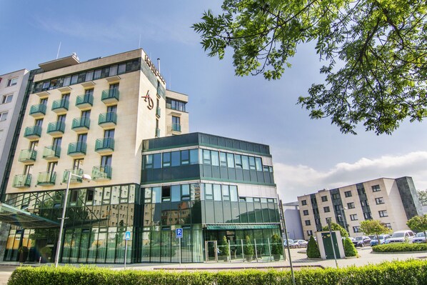 A modern hotel with a glass facade, multiple balconies, and a clear view of the surrounding urban area. - Alexandra Business Hotel (Puchov)