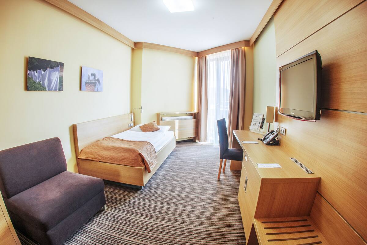 A hotel room with a bed, a desk, a chair, and a television.