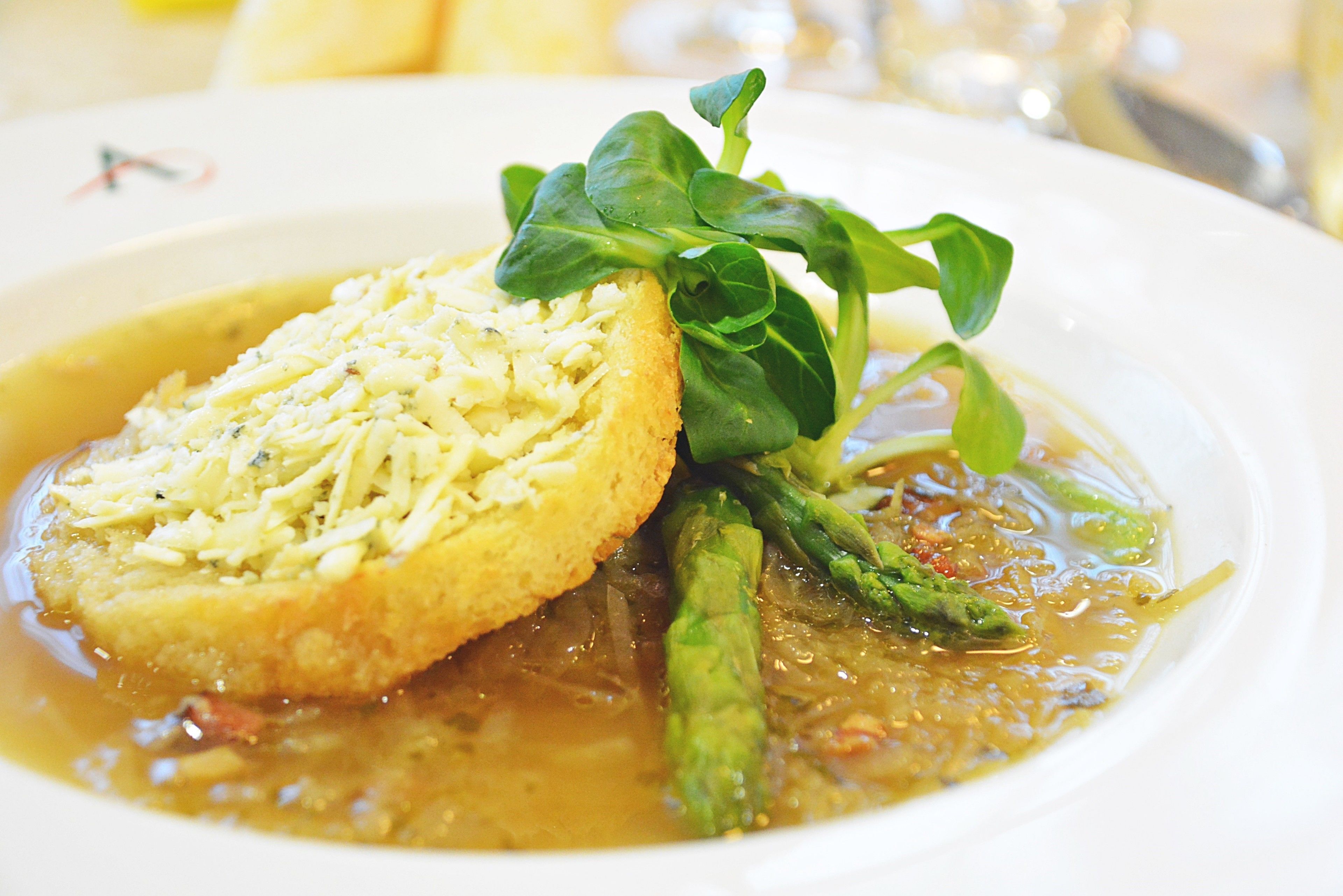 A bowl of soup with a piece of bread and asparagus.