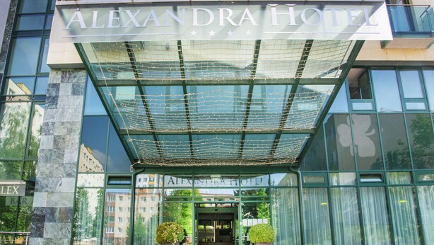 Exterior do Hotel Alexandra, com fachada de vidro moderna, entrada coberta e porta de acesso visível.