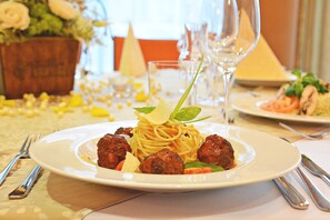 A dining table with a plate of spaghetti with meatballs, a glass of wine, and a vase of flowers. - Alexandra Business Hotel (Puchov)