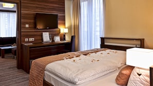 Quarto de hotel com cama, escrivaninha com computador, televisão fixada na parede e janela com cortinas.