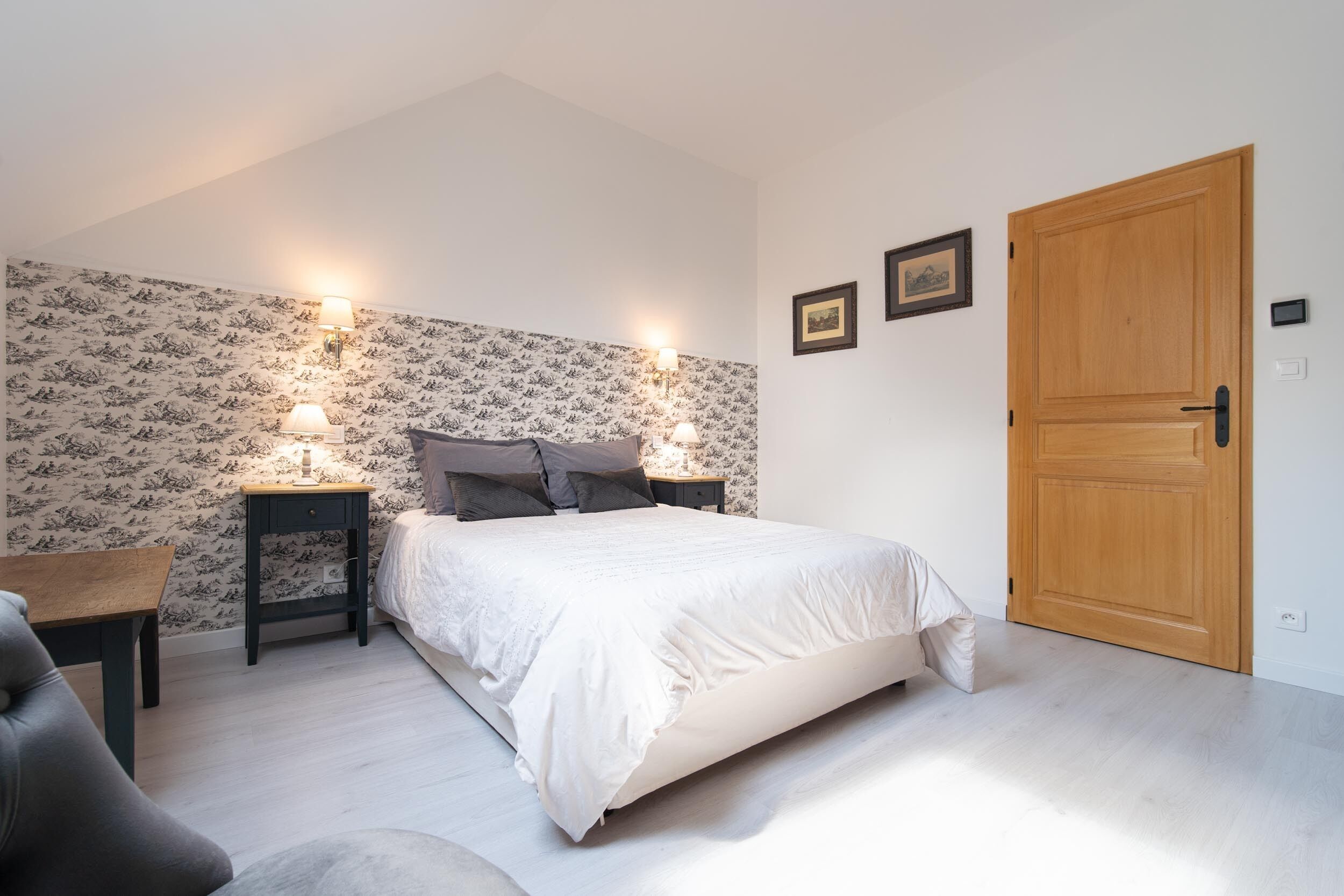 A bedroom with a bed, two bedside tables with lamps, a wooden door, and a patterned wallpaper.