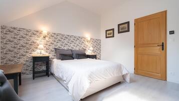 A bedroom with a bed, two bedside tables with lamps, a wooden door, and a patterned wallpaper.