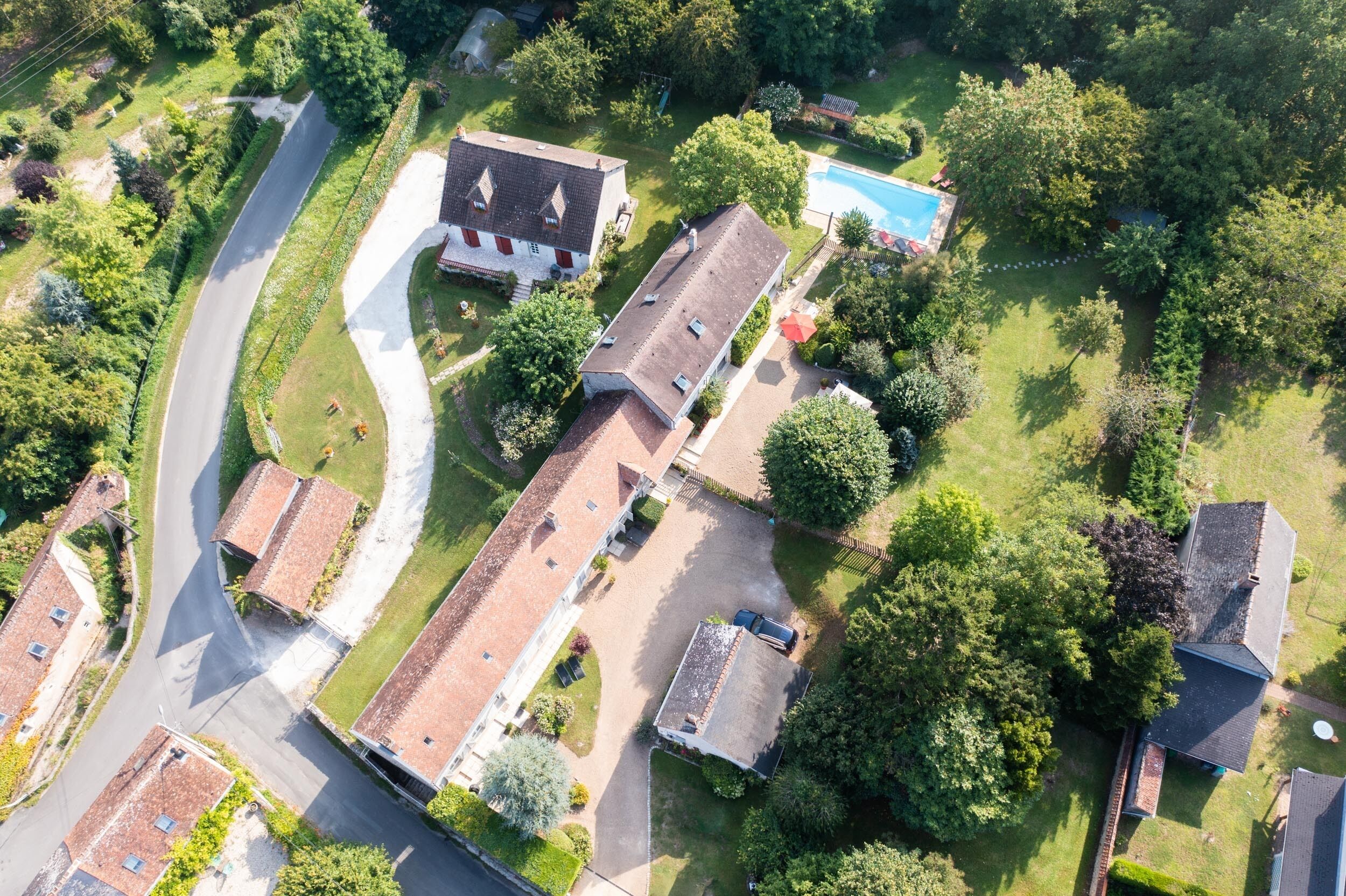 An aerial view of a residential area with multiple houses, a swimming pool, and a curved road.