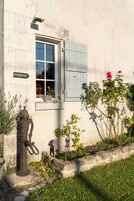 Un bâtiment avec une pancarte indiquant « PARKING », une fenêtre avec des volets bleus et un petit jardin agrémenté de plantes et d’une structure métallique décorative.