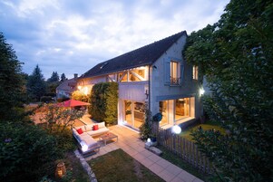 Une maison à deux étages avec un patio, un parasol rouge et un canapé blanc.