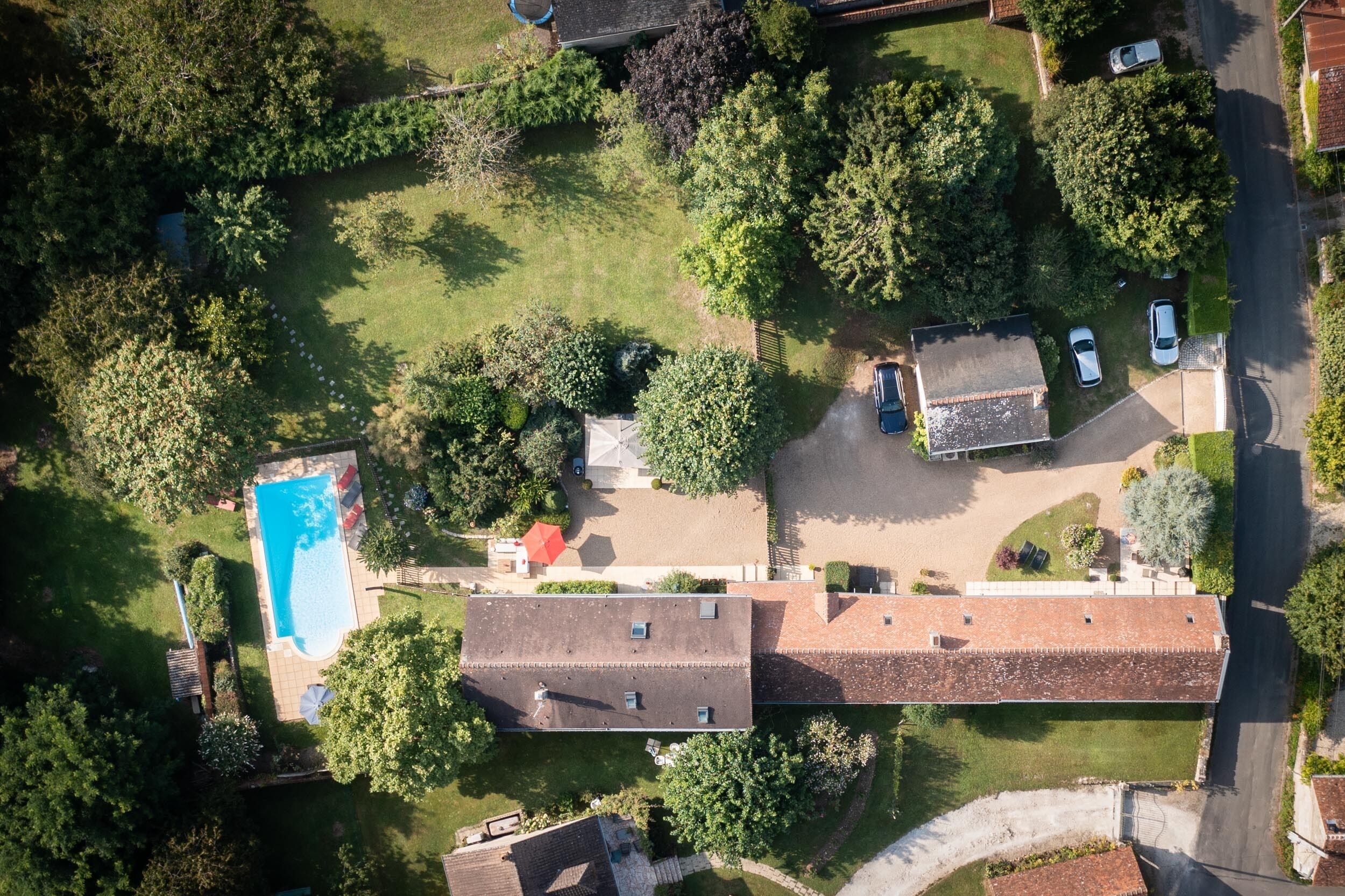 Ovenfra ses et boligområde med en swimmingpool, flere huse og en vej.