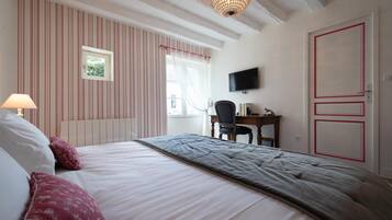 A bedroom with a bed, a desk, a chair, a television, and a window with curtains.
