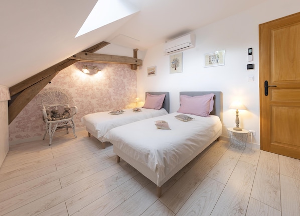 A bedroom with two beds, a wooden chair, a skylight, and a wooden door.