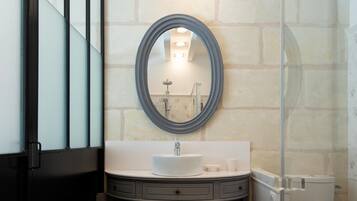A modern bathroom with a glass shower enclosure, a round mirror, and a vanity with a sink and drawers.