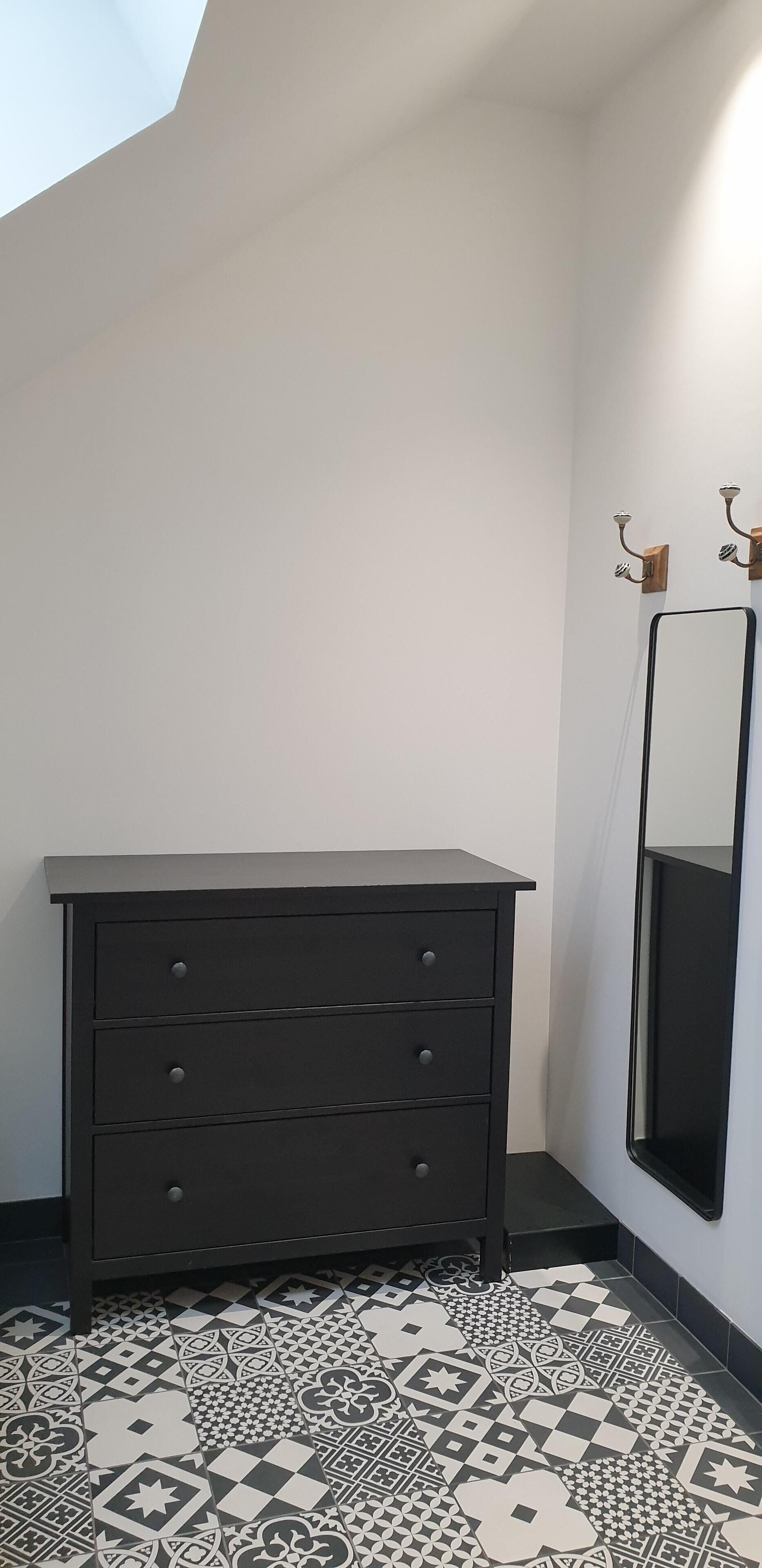 Een kamer met een donkere dressoir, een vloer met patroon, een spiegel aan de muur, en een lamp.