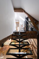 Un escalier moderne avec des rampes en verre et des éléments décoratifs en bois, menant à un espace repas comprenant une table et des chaises.