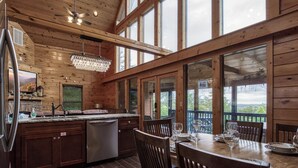 A wooden cabin interior with a kitchen, dining area, and large windows offering views of the outdoors. - Secluded cabin-Movie theater, outdoor kitchen and outdoor tv- Mountain View-gameroom (SEVIERVILLE)