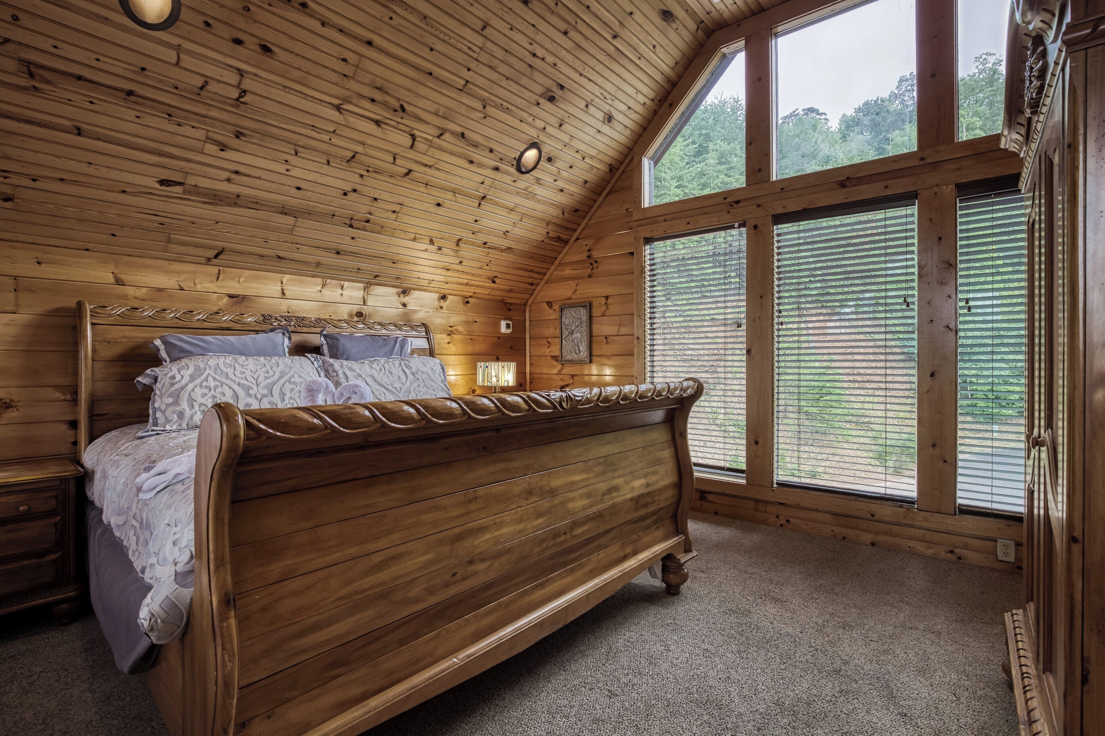 Een slaapkamer met houten details, een groot bed, een nachtkastje en een raam met jaloezieën.