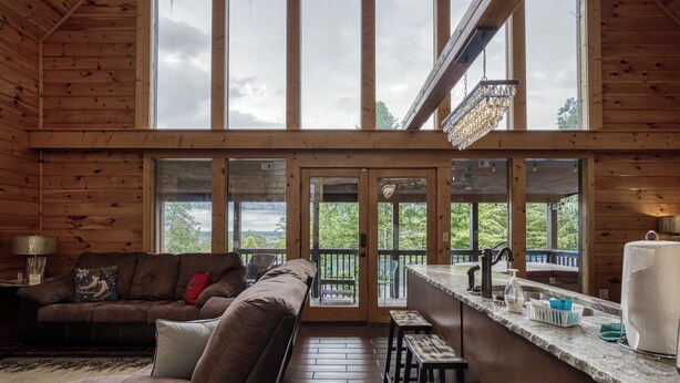 A wooden cabin interior with a sofa, a dining area, and large windows offering a view of greenery. - Secluded cabin-Movie theater, outdoor kitchen and outdoor tv- Mountain View-gameroom (SEVIERVILLE)