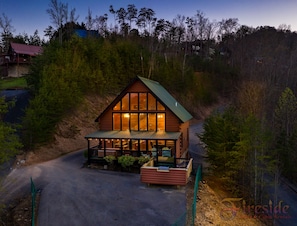 Situated in a forest, this cabin offers a porch area and a driveway leading to its entrance.