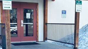 Une entrée d’immeuble avec une enseigne indiquant « RÉSIDENCES THREE SEASONS », un panneau indiquant une zone de chargement/déchargement et un panneau de stationnement réservé aux personnes handicapées.