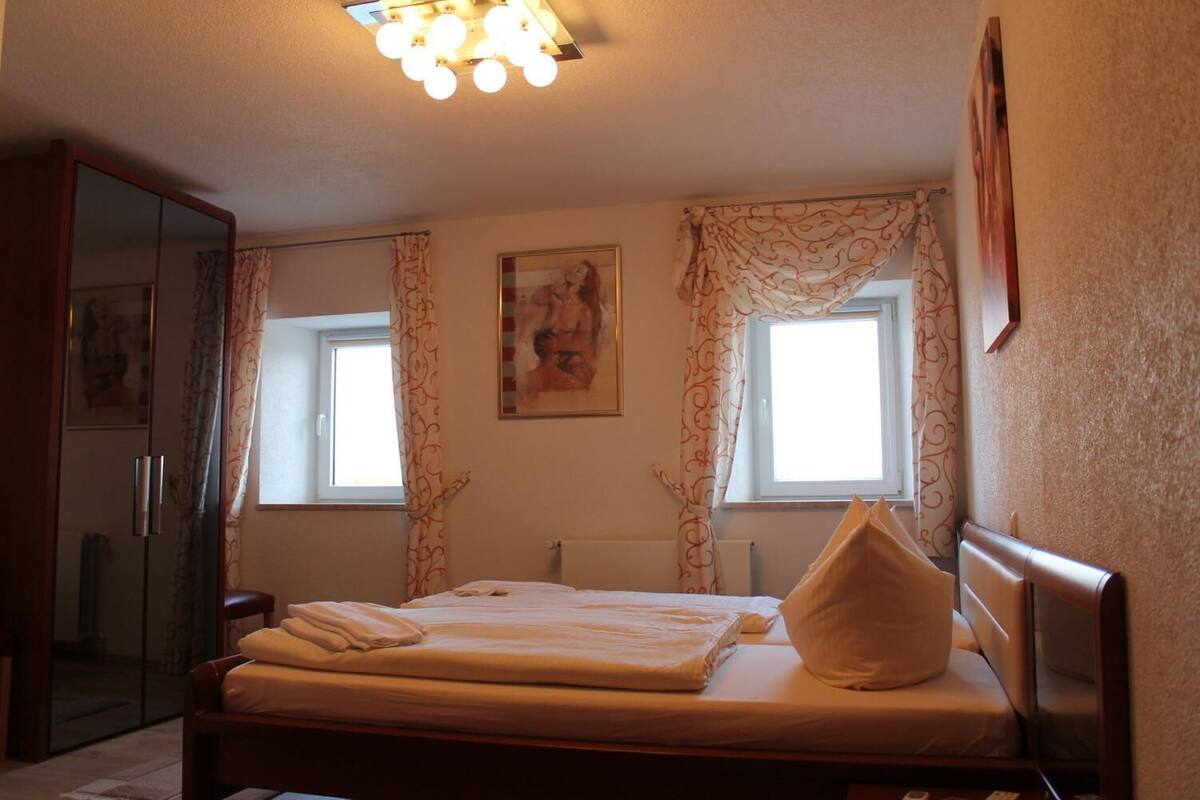 A bedroom with a bed, a wardrobe, a radiator, and a window with curtains.