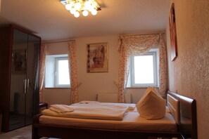 A bedroom with a bed, a wardrobe, a radiator, and a window with curtains. - Landhotel Fuchsbau (Vohenstrauss)