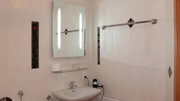 A bathroom with a white sink, a mirror, a towel rack, and a shower area.