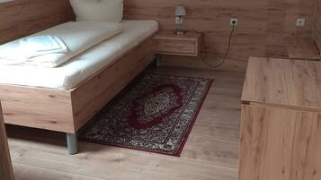 Un dormitorio con una cama de madera, una mesita de noche con lámpara, un tapete rojo estampado y un pequeño aparador de madera.