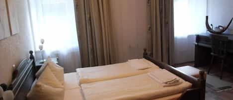 Una cama doble con dos almohadas, un escritorio con una silla y una ventana con cortinas.