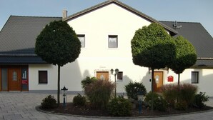 Un edificio con facciata simmetrica, due alberi di fronte e un cortile lastricato.