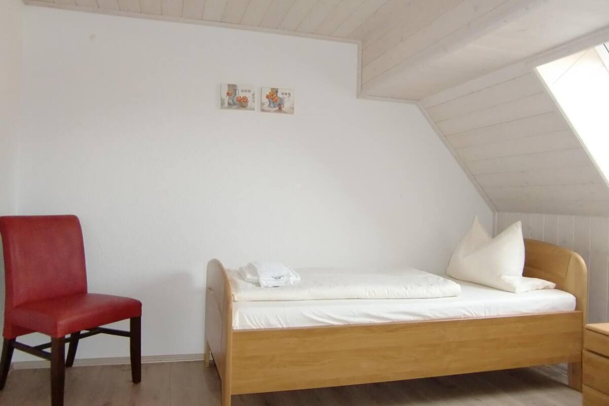 A room with a wooden bed, a red chair, and a sloped ceiling with a skylight.