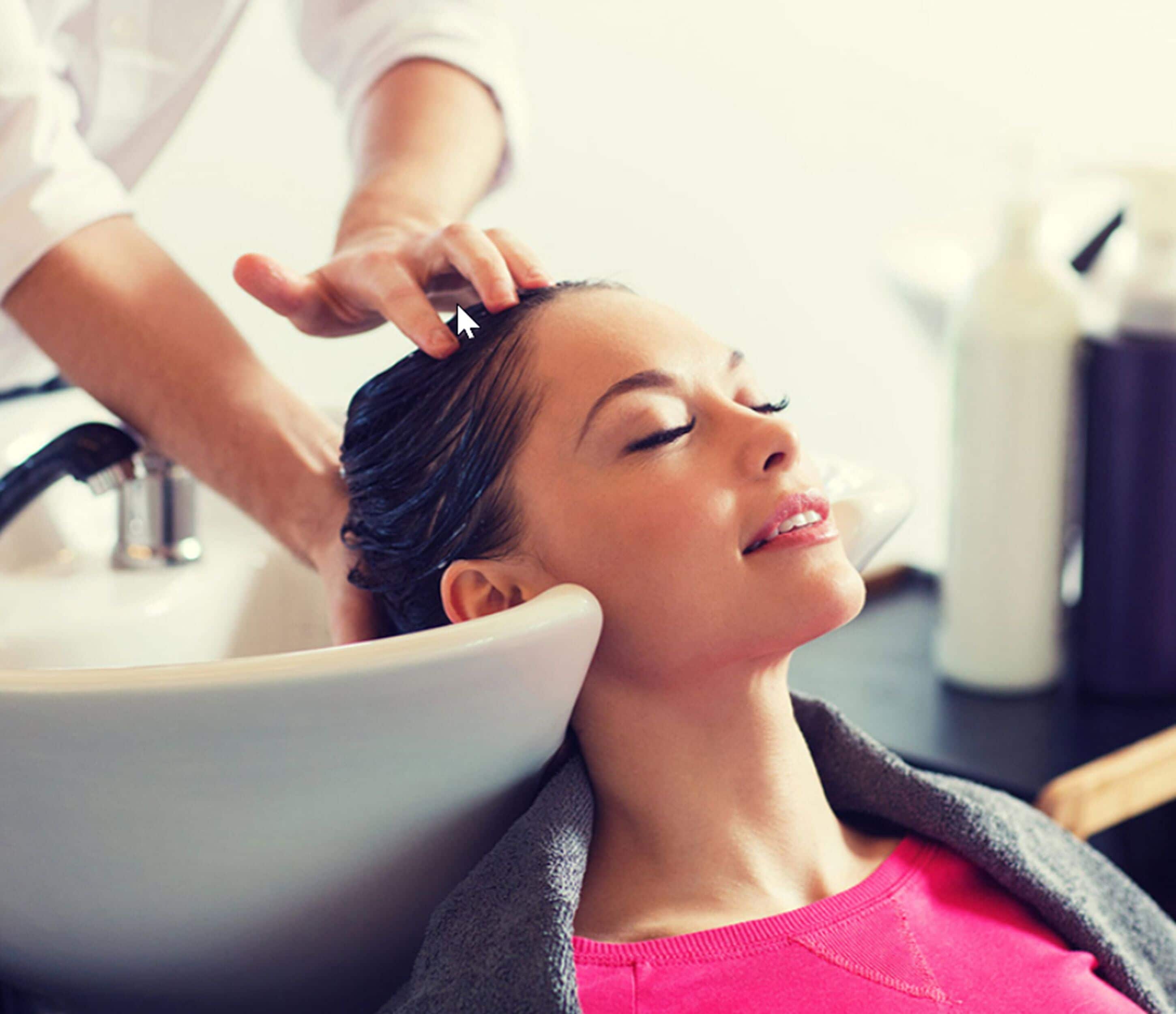 A person receiving a hair treatment in a bathroom with a sink and toiletries visible.