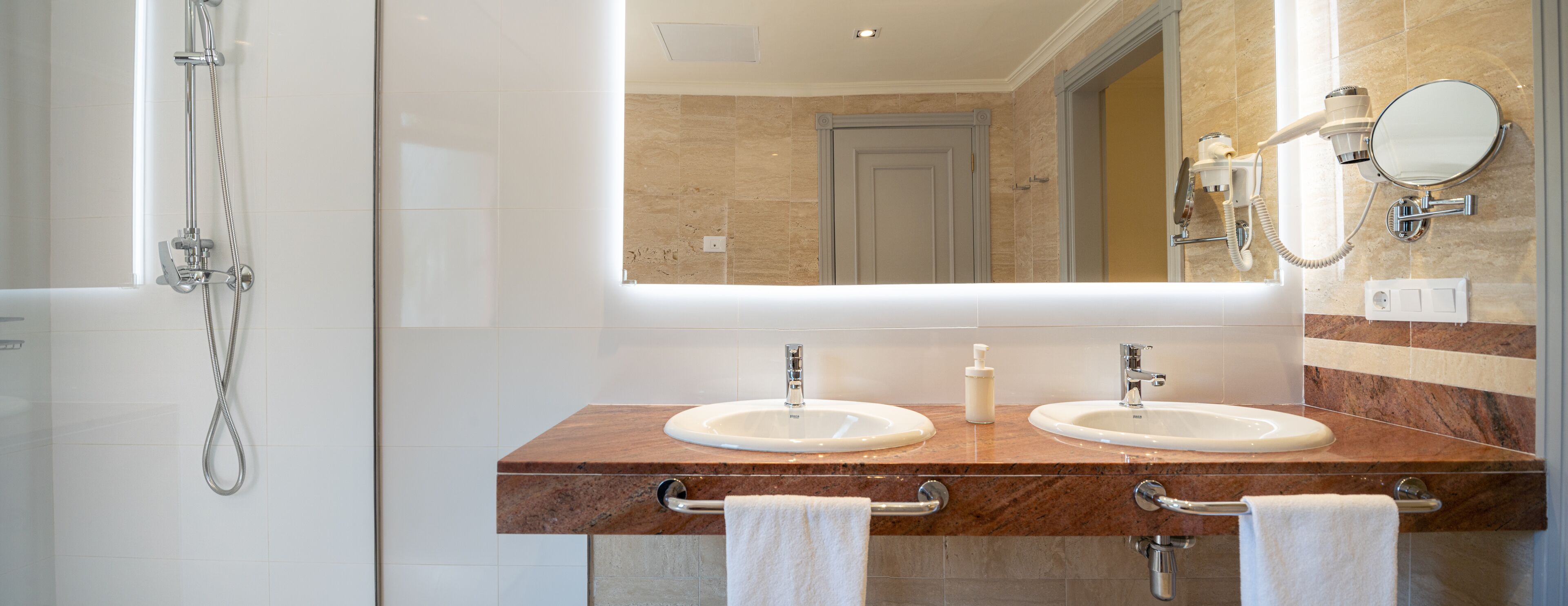 Een badkamer met twee wasbakken, een spiegel, een haardroger en een douche.