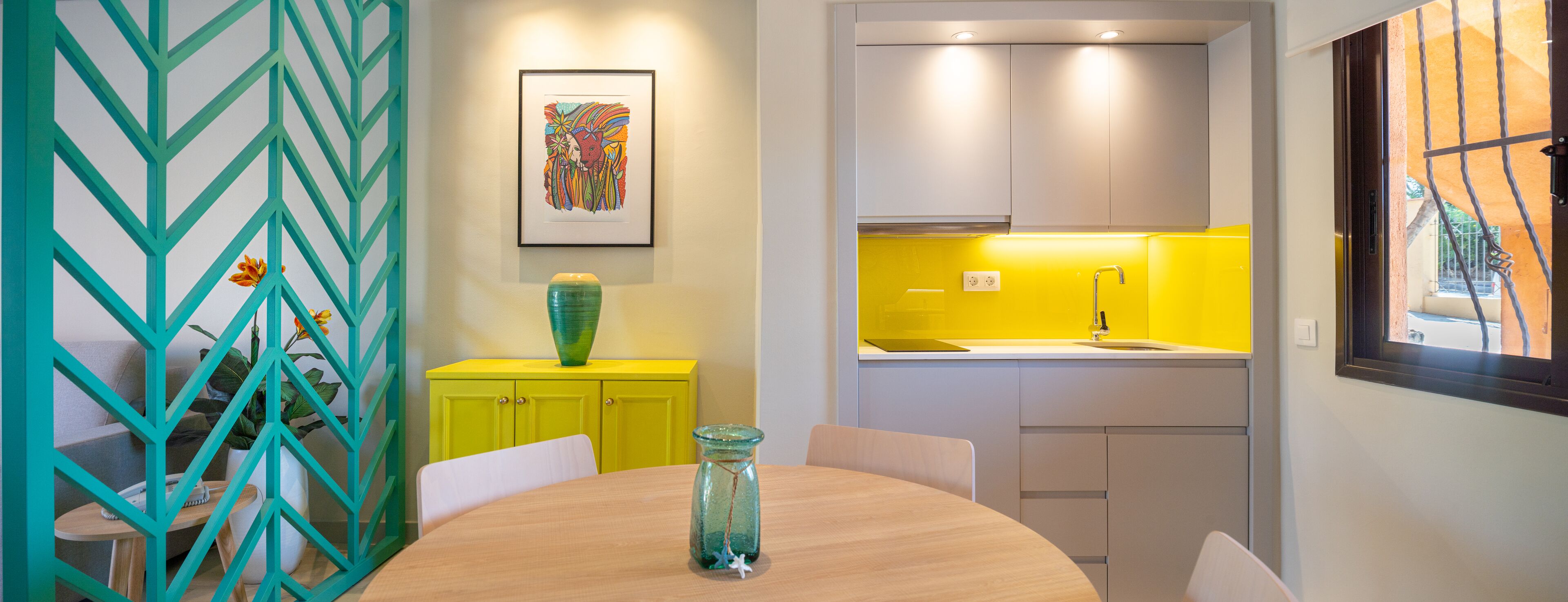 Une cuisine moderne avec un mur de fond jaune, un coin repas doté d’une table ronde et un séparateur décoratif de couleur turquoise.