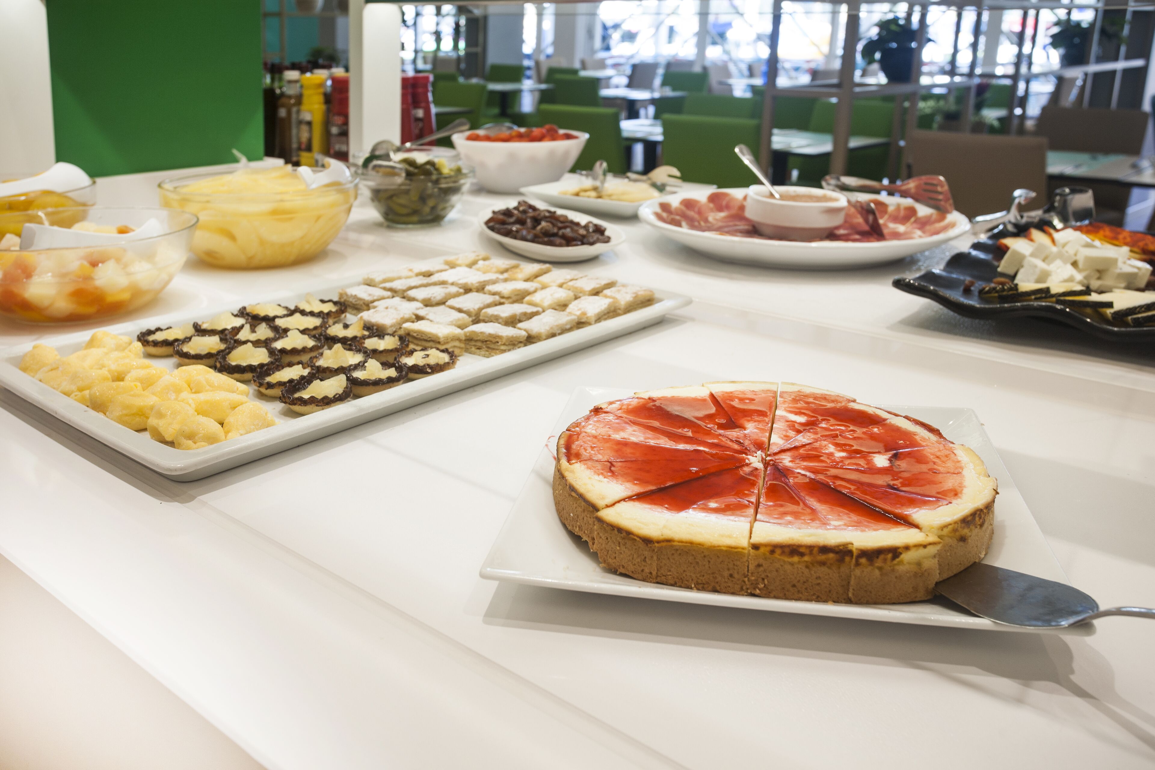 Une table de buffet proposant divers plats, notamment un grand gâteau au fromage, des fruits et d’autres desserts.