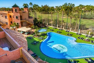 Un resort con una amplia piscina, tumbonas y un campo de golf al fondo.
