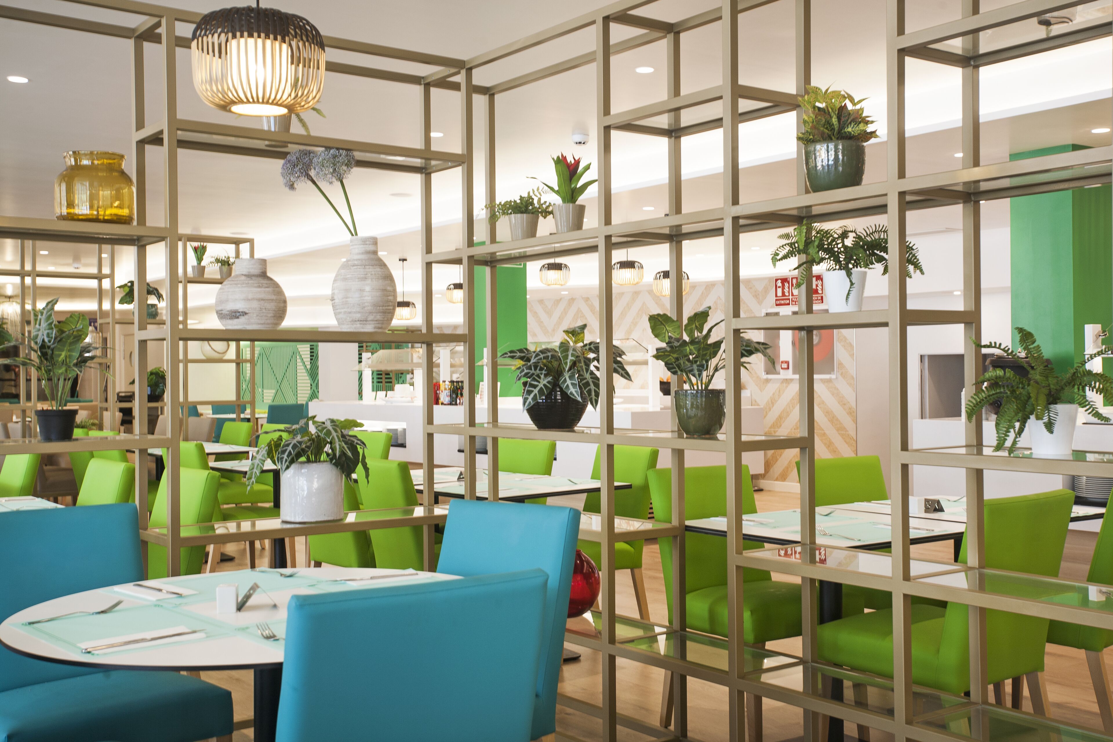 Un restaurant avec des chaises et des tables vertes, des plantes en pot et un décor intérieur moderne.