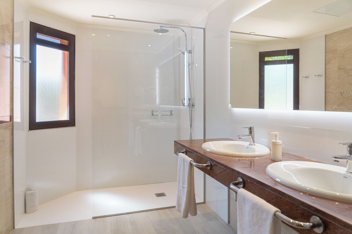 A modern bathroom with a glass-enclosed shower, a vanity with a sink and mirror, and a towel rack.