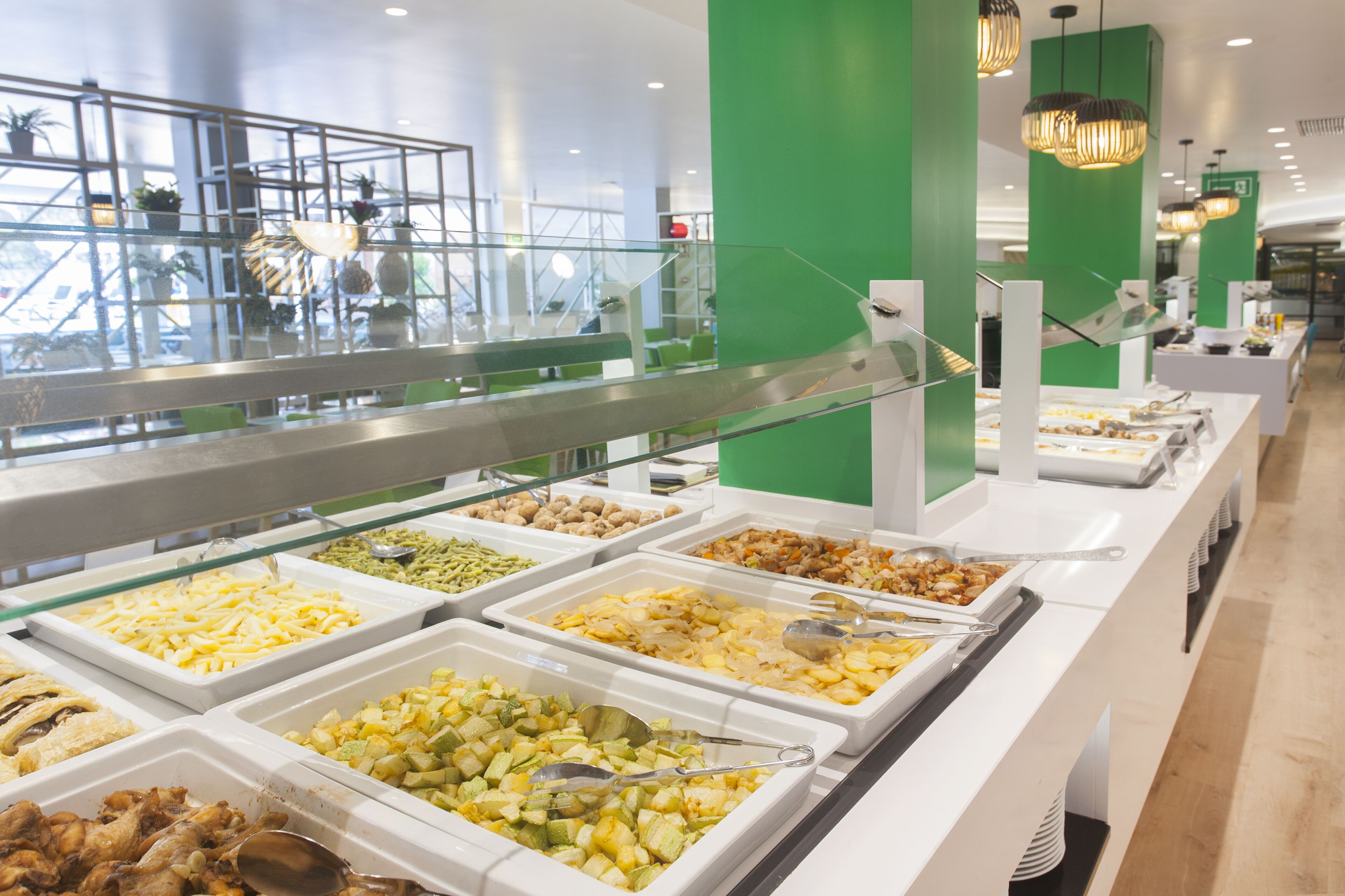 Buffet com diversas opções de comida, guarda-corpo de vidro e uma parede verde de destaque.