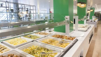 Buffet com diversas opções de comida, guarda-corpo de vidro e uma parede verde de destaque.