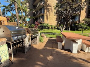 Ein Grill und eine Sitzgelegenheit im Freien mit Blick auf ein mehrstöckiges Gebäude und Palmen.