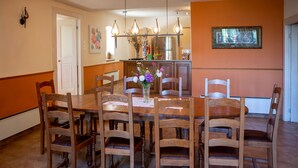 Un comedor con una mesa y sillas de madera, un jarrón con flores y una cocina al fondo.