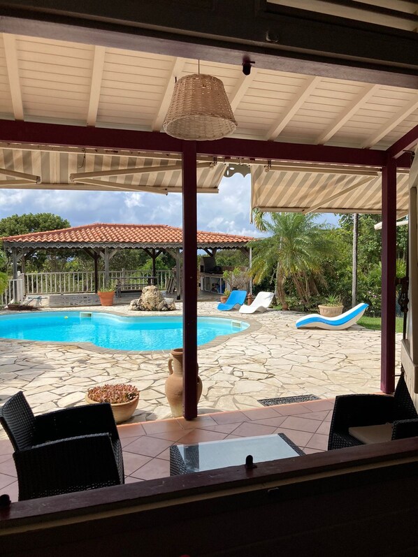 A covered outdoor area with a pool, lounge chairs, and a view of a building with a tiled roof. - Villa Mahogany and its bungalow in Sainte Anne (Sainte Anne)