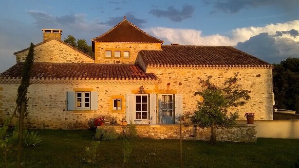 A stone building with a tiled roof, a central door, and a small porch area.